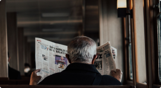 A reader with a broadsheet newspaper open in front of a shopfront