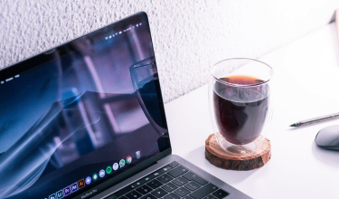 A laptop, a glass of coffee and a pen on a studio desk