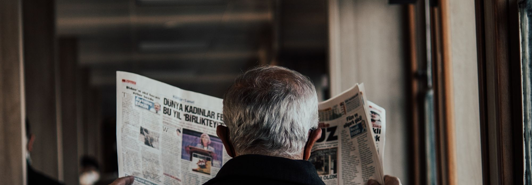 A reader with a broadsheet newspaper open in front of a shopfront