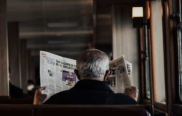 A reader with a broadsheet newspaper open in front of a shopfront