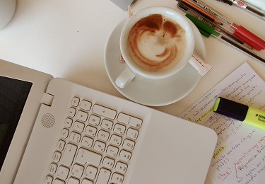 A keyboard, a cup of coffee and an annotated page on a desk